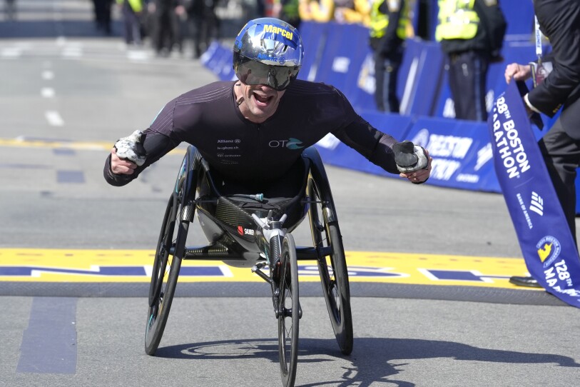 Wheelchair athlete Marcel Hug smiles and cheers as he breaks through the ribbon at the finish line of the Boston Marathon.